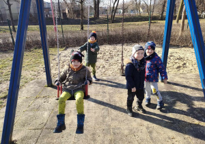 Kilkoro dzieci z grup: "Skrzatów" i "Biedronek" na huśtawkach na placu zabaw w Parku Miejskim.