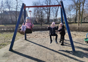 Trzy dziewczynki na huśtawkach na placu zabaw w Parku Miejskim.