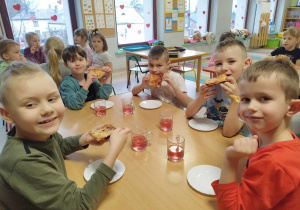 Dzieci jedzą przygotowaną przez siebie pizzę.