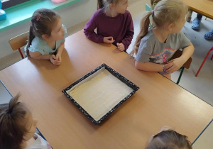 Dzieci słuchają instrukcji nauczyciela dotyczących przyrządzenia pizzy.