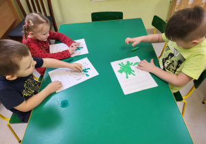 Kilkoro dzieci przy stole podczas pracy plastycznej, opartej na wyklejaniu kolorową plasteliną szablonu glutka.