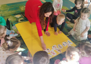 Dzieci siedzą na dywanie i nazywają czynności dzieci na ilustracjach.