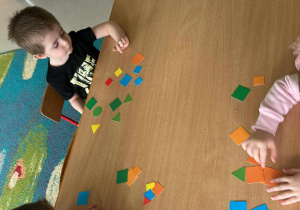 Kilkoro dzieci przy stoliczku w trakcie matematycznych zabaw z kolorowymi figurami geometrycznymi.