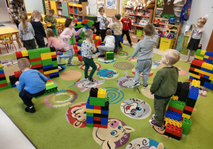 Dzieci z grupy "Pszczółek" podczas zajęć z ogromnymi, kolorowymi klockami LEGO.