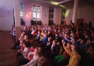 Dzieci siedzą na krzesełkach i aktywnie biorą udział w musicalu pt. "Przybysze z Planety Zangular".