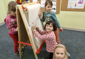 Zuzia, Ala i Marysia rysują kolorowymi mazakami na dużym formacie białego papieru.