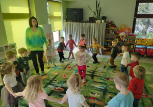 Dzieci z grupy maluszków tańczą w kole. W środku koła stoi Mariczka z opaską papryki.