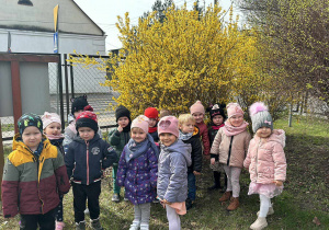 Dzieci z grupy "Żabek" pozują do pierwszego, wiosennego zdjęcia grupowego na tle ogrodu przedszkolnego.