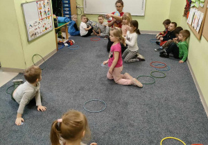 Ciocia Justynka tłumaczy dzieciom zasady zabawy orientacyjno-porządkowej "Tańczące jajka". Dzieci, które mają taki wzór pisanki, dobierają się w grupę.