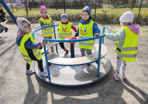 Kilkoro dzieci na karuzeli na placu zabaw w Parku Miejskim.