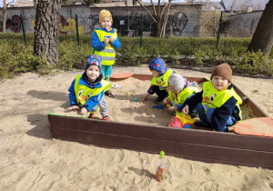 Kilkoro dzieci bawi się w piaskownicy na placu zabaw w Parku Miejskim.