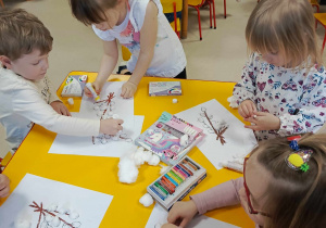 Czworo dzieci z "Motylków" tworzy kuleczki z waty i przykleja je na szablon.