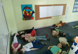 Dzieci leżą na dywanie na plecach i słuchają dźwięków lasu.