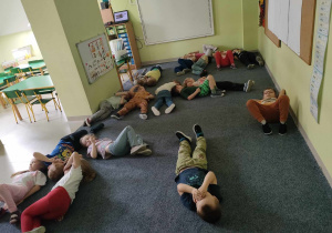 Dzieci leżą na dywanie na plecach i słuchają dźwięków lasu.
