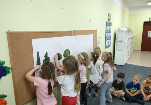 Dziewczynki przyczepiają ilustracje drzew na makietę.