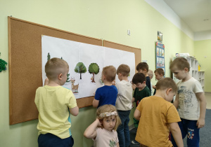 Chłopcy przyczepiają ilustracje zwierząt leśnych na makiecie.