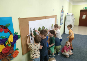 Chłopcy przyczepiają ilustracje darów lasu na makiecie.