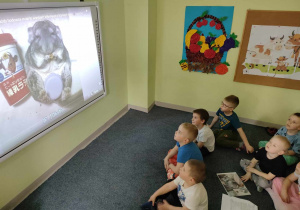 Dzieci z grupy "Pszczółek" oglądają film edukacyjny o szynszylach na tablicy interaktywnej.