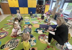 Dzieci z grupy "Motylków" siedzą na dywanie i uważnie słuchają cioci Oli z biblioteki.