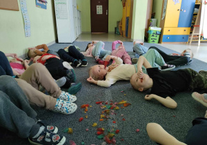 Dzieci uczestniczą w zabawie - "Piórkowe wyciszanki". Leżą na plecach, słuchają dźwięków lasu i smyrają się piórkiem po buzi.