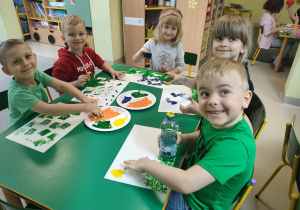 Kilkoro dzieci przy stoliku podczas twórczej pracy z wykorzystaniem wybranego zużytego przedmiotu oraz farby.