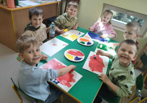 Kilkoro dzieci przy stoliku podczas twórczej pracy z wykorzystaniem wybranego zużytego przedmiotu oraz farby.