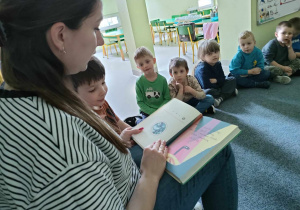 Pani Kamilka trzyma w dłoniach i czyta książkę pt. "Niesamowite przygody dziesięciu skarpetek", autorstwa Justyny Bednarek.