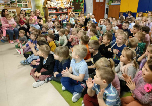 Dzieci siedzą na dywanie i z ogromną uwagą słuchają brzmienia tuby.