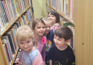 Dzieci spacerują pomiędzy regałami z książkami.
