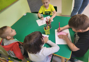 Kilkoro dzieci z grupy "Pszczółek" przy stoliku ozdabia szablon książki wg własnego pomysłu.