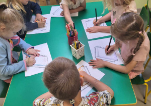 Kilkoro dzieci z grupy "Pszczółek" przy stoliku ozdabia szablon książki wg własnego pomysłu.