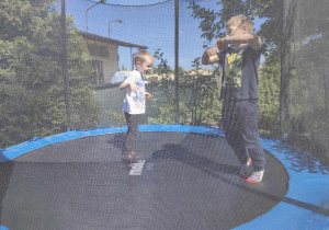 Adam i Alan skaczą na trampolinie.