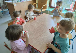 Kilkoro dzieci z grupy "Żabek" przy stoliku, podczas degustacji pysznego, naturalnego soku jabłkowo-marchewkowego z dodatkiem cytryny i miodu.