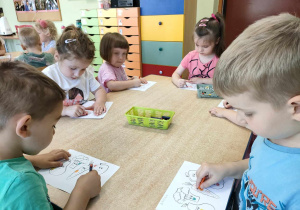 Kilkoro dzieci z grupy "Żabek" przy stoliku starannie koloruje szablon owoców i warzyw zgodnie z ich kolorystyką.