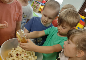 Antoś dodaje miodu akacjowego do sałatki owocowej.