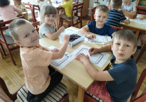 Kilkoro dzieci przy stoliku rysuje rzeczy potrzebne ich zdaniem na wakacyjną podróż.