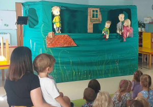 Dzieci oglądają przedstawienie. Przed nimi stoi scena, na której rozgrywa się akcja spektaklu.