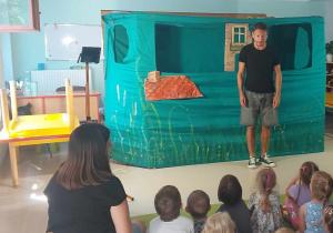 Mężczyzna stoi przed dziećmi, wita się z nimi i rozpoczyna przedstawienie.