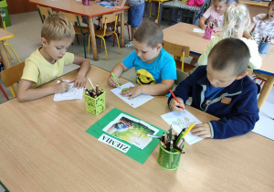 Troje dzieci siedzi przy stoliku, kolorując odpowiedni szablon związany z żywiołem ziemi.