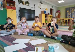 Dzieci siedzą w kole i piją wodę z kubków.