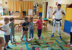 Dzieci z grupy "Biedronek" z uwagą patrzą na sensei'a, który pokazuje pierwszy ruch karate.