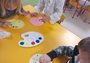 Troje dzieci z grupy "Żabek" podczas pracy plastycznej, opartej na stemplowaniu paluszkiem szablonu balona.