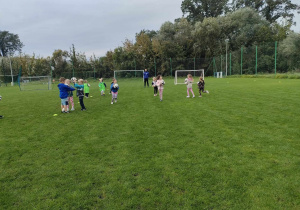 Dzieci z grupy "Pszczółek" podczas zabawy w "Berka" z piłkami na boisku sportowym.