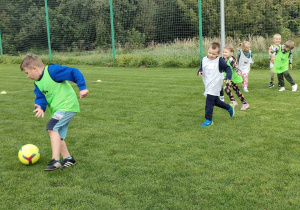 Kilkoro dzieci z grupy "Pszczółek" podczas meczu piłki nożnej na boisku sportowym.