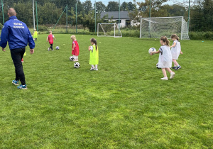 "Motylki" uczą się prowadzenia piłki po boisku sportowym.