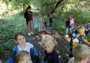 Przedszkolaki sprzątają teren Parku Miejskiego wzdłuż ścieżki.