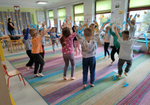 Zabawy ruchowe z niebieskimi wstążkami na dywanie wśród dzieci z grupy "Pszczółek".