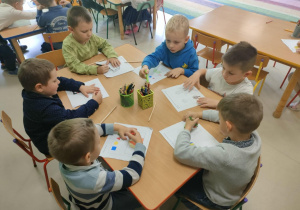 Kilkoro dzieci przy stoliku podczas rozwiązywania wybranych przez siebie zadań, opartych na ćwiczeniu logicznego myślenia i skupieniu uwagi.