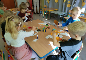 Przyklejamy włoski z bibuły w kolorach, symbolizujących ogień oraz rysujemy mazakiem elementy twarzy.