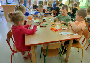 Przyklejamy włoski z bibuły w kolorach, symbolizujących ogień oraz rysujemy mazakiem elementy twarzy.